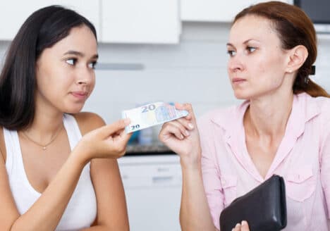 eine Mutter gibt ihrer Tochter 20 Euro und schaut sie mit einem kritischen Blick an