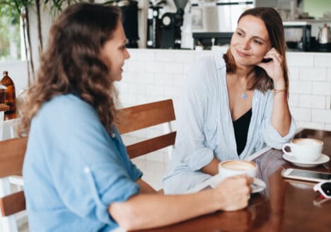 zwei Frauen sitzen sich in einem Kaffee gegenüber. Die eine erzählt etwa und die andere hört zu