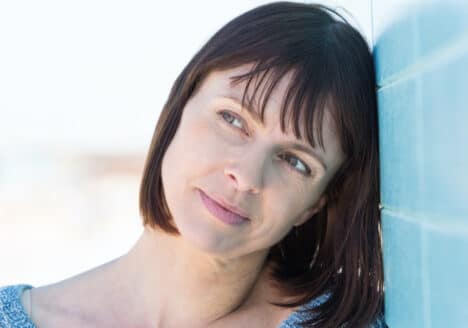 eine Frau hat den Kopf an der Wand angelehnt und schaut nachdenklich in die Leere