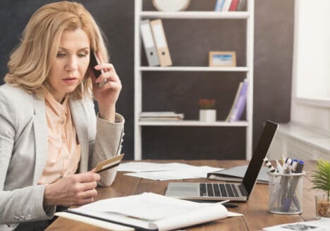eine Frau sitzt am Schreibtisch und telefoniert mit dem Handy am Ohr